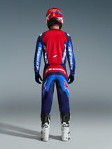 Alpinestars 2026 Fluid Grid-sæt, motocross-kører set bagfra iført komplet racerudstyr, Fluid Grid-bukser i Blue Red, matchende rød og blå trøje med Alpinestars-branding, rød og blå hjelm, hvide og sorte støvler, koordineret outfit til off-road racing