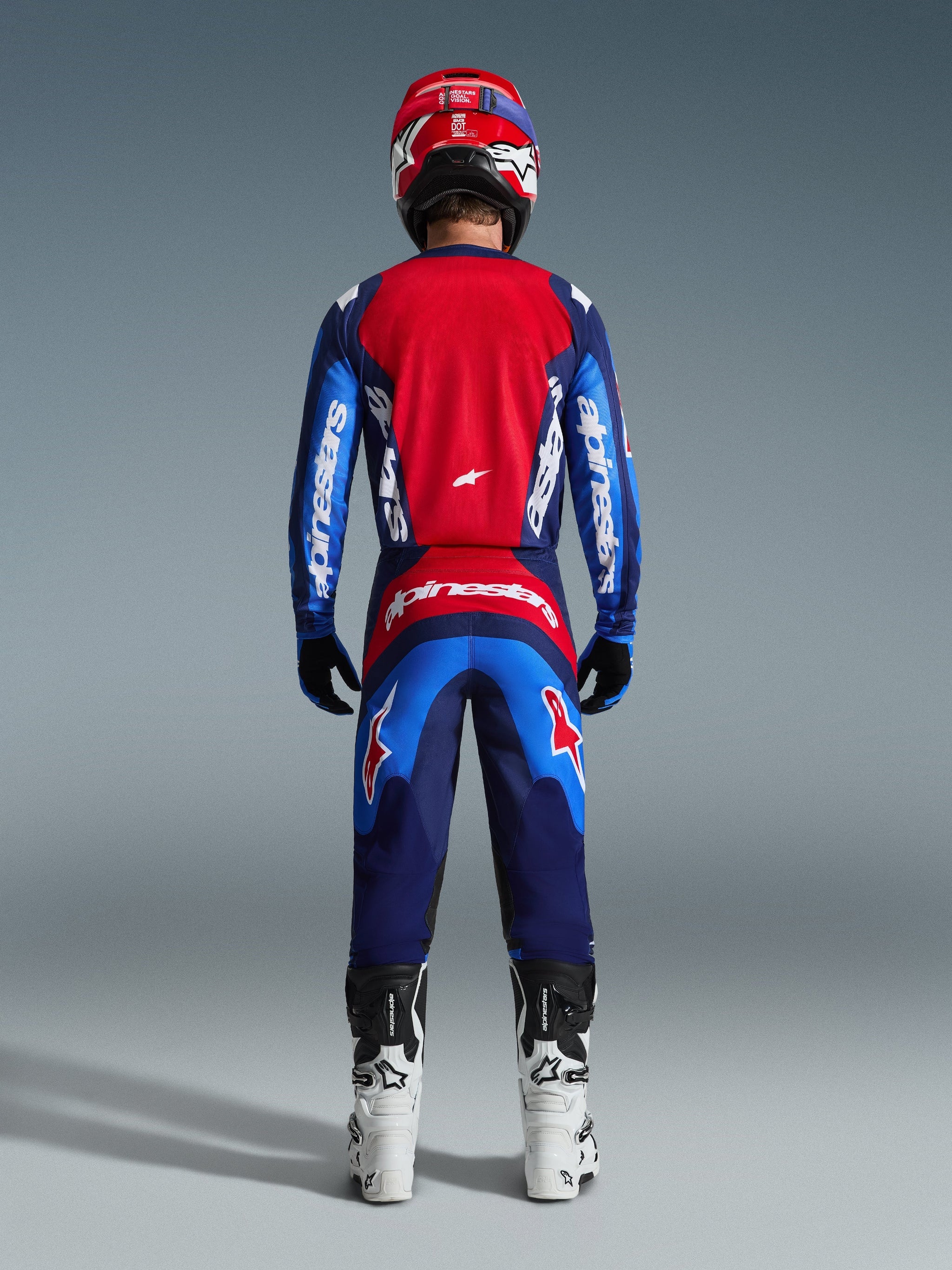 Alpinestars 2026 Fluid Grid-sæt, motocross-kører set bagfra iført komplet racerudstyr, Fluid Grid-bukser i Blue Red, matchende rød og blå trøje med Alpinestars-branding, rød og blå hjelm, hvide og sorte støvler, koordineret outfit til off-road racing
