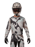 Alpinestars 2024 Racer Tactical trøje, motocross-trøje, Iron Camo Dust Gray kamuflage-mønster, kører iført matchende hjelm og beskyttelsesbriller med sorte handsker, teknisk udstyr til off-road racing