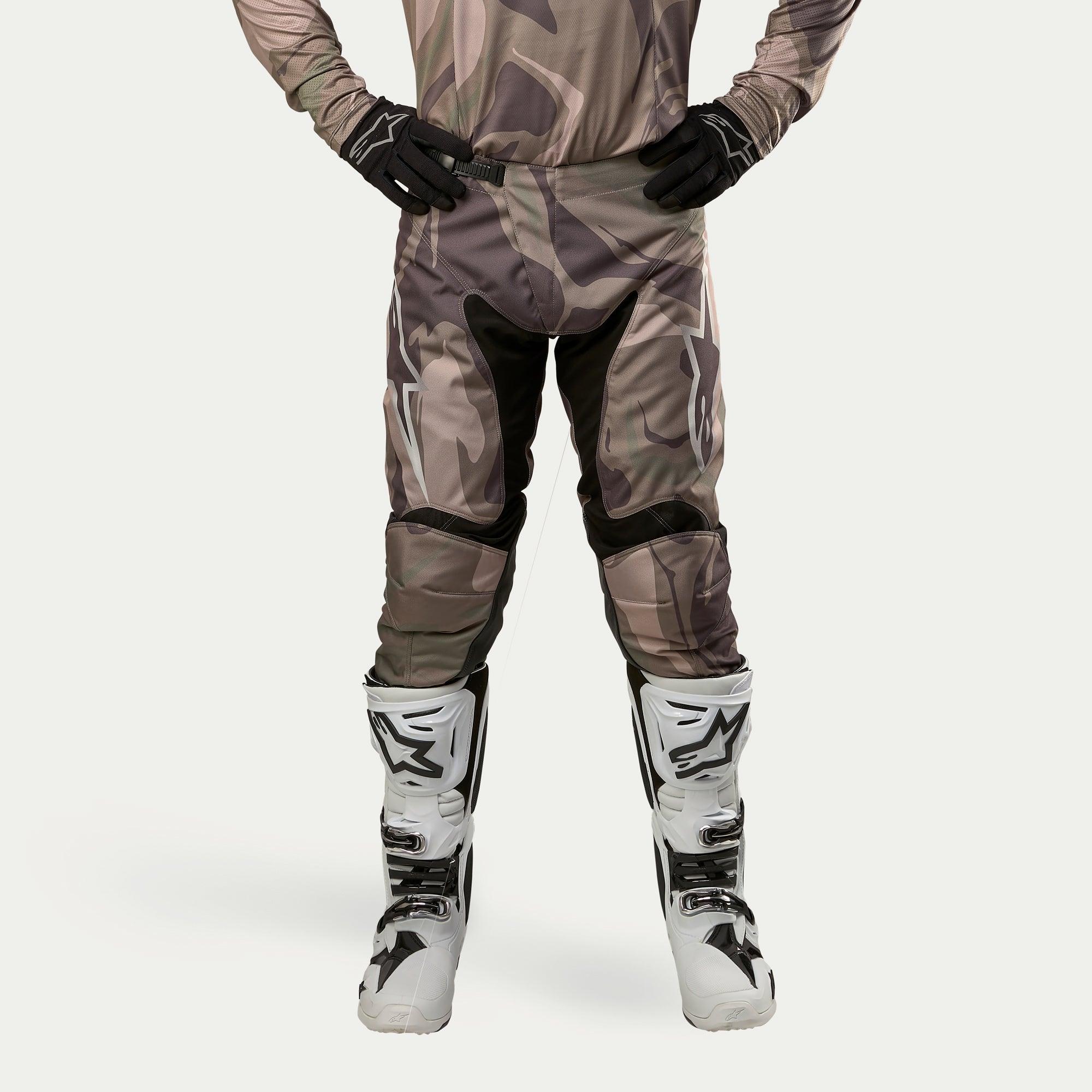Alpinestars 2024 Racer Tactical bukser, motocross-bukser, militærgrøn camouflage-brun, med store hvide Alpinestars-logoer på lårene og sorte paneler på indersiden af benene, båret med hvide og sorte motocross-støvler, sorte handsker og matchende camouflage-trøje, set forfra.