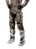 Alpinestars 2024 Racer Tactical bukser, motocross-bukser, militærgrøn camouflage-brun, båret med matchende camouflage-jersey, sorte handsker og hvide støvler med stjerne-logoer, sorte strækpaneler og ergonomisk design, off-road udstyr på hvid baggrund