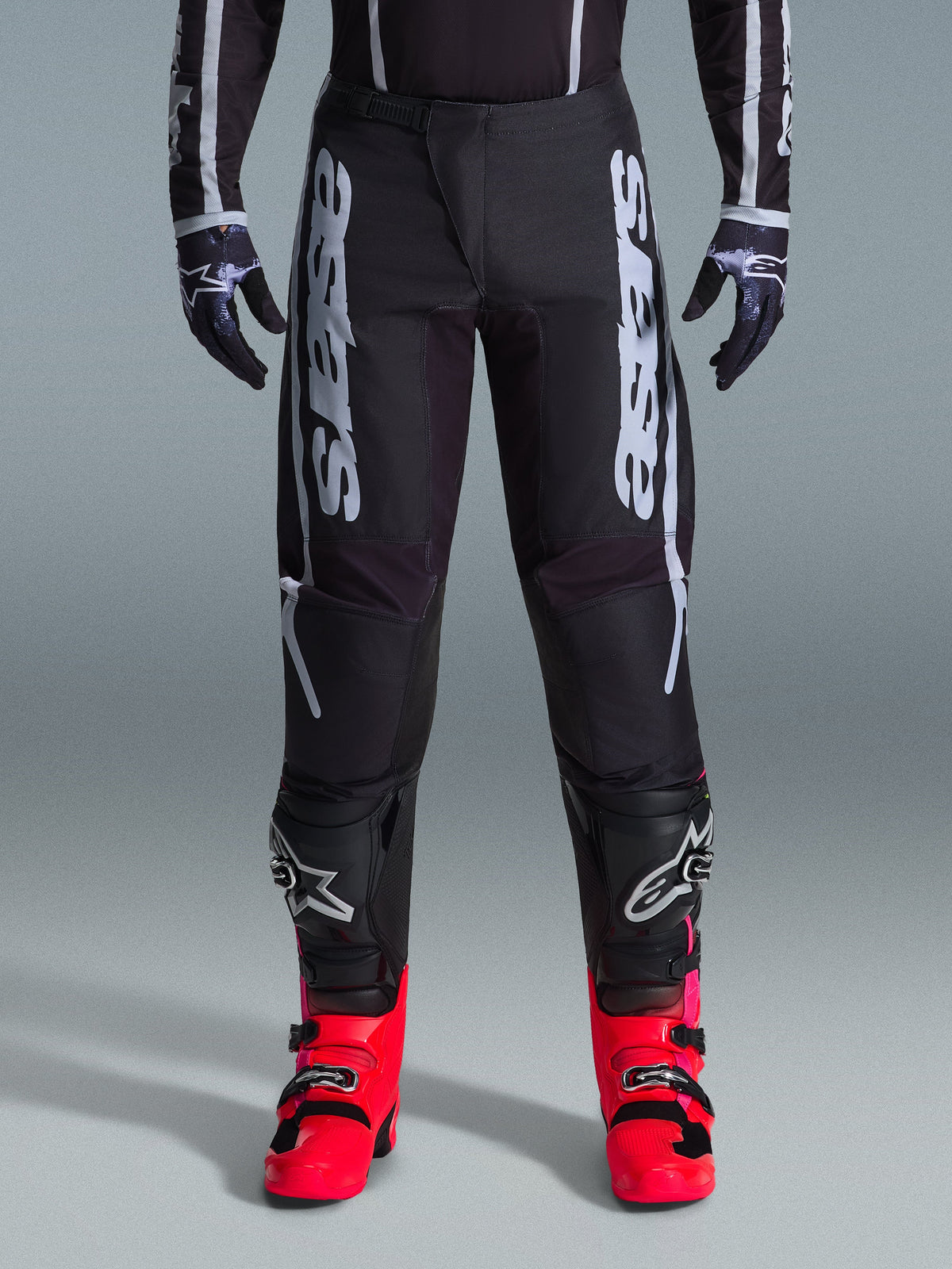 Alpinestars 2026 Fluid Apex bukser, sorte motocrossbukser med stor hvid tekst, båret med sort knæbeskyttelse og markante røde støvler, letvægts 600D polyfabric-chassis, sport-fit design til off-road racing