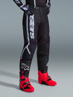 Alpinestars 2026 Fluid Apex bukser, motocross-bukser, sort og grå, båret med livlige pink og røde støvler og matchende sort og hvid trøje, med markant lodret Alpinestars-branding på låret, forstærkede paneler og skraldelukning i taljen for off-road ydeevne.