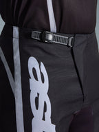 Alpinestars 2026 Fluid Apex bukser, motocrossbukser, sort og grå, nærbillede af det integrerede skraldelukningssystem for en sikker pasform, med hvid logografik på slidstærkt 600D polystof.