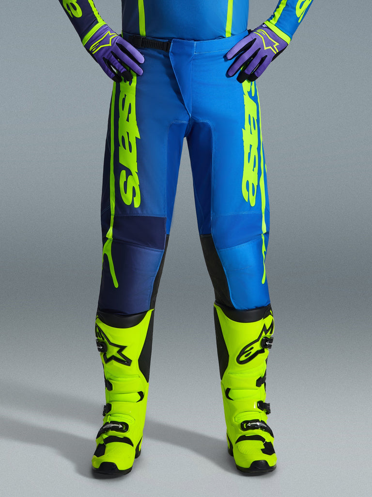 Alpinestars 2026 Fluid Apex bukser, motocrossbukser, blå og gul fluo, vist med matchende fluogule støvler og lilla handsker, markant gul branding på siderne, ergonomisk design til off-road-racing