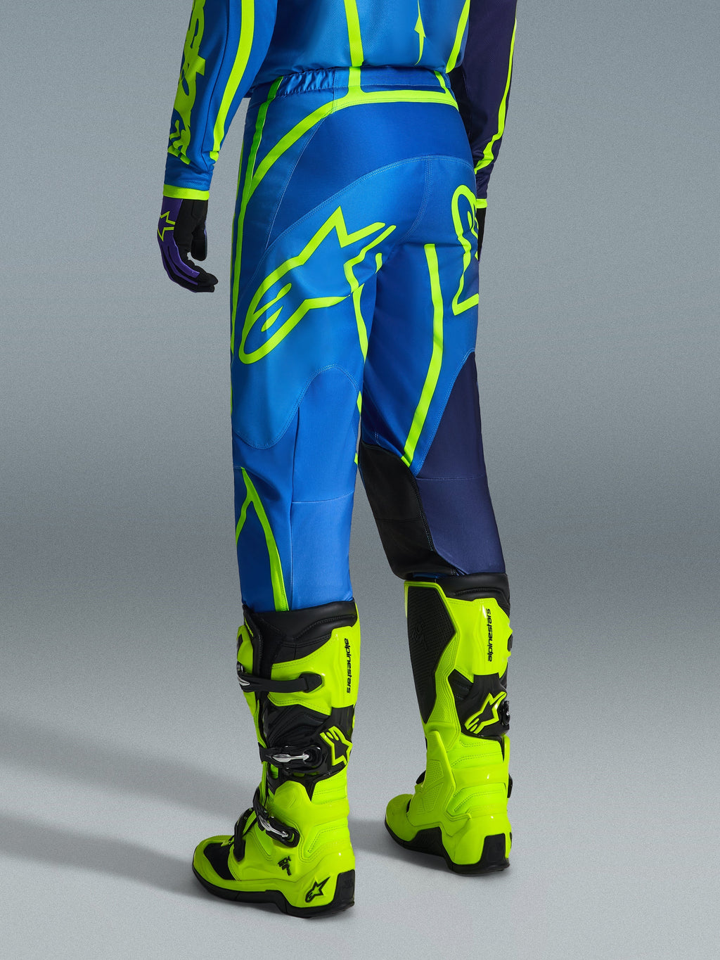 Alpinestars 2026 Fluid Apex bukser, motocrossbukser, blå og neongul, set bagfra af en kører i matchende udstyr og neongule støvler, med markante Alpinestars-logoer og ergonomisk design
