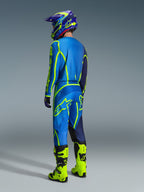 Motocross-kører set bagfra iført 2026 Alpinestars Fluid Apex bukser i blå og neon-gul, matchende blå og gul trøje og hjelm, samt klare neon-gule støvler, koordineret racerudstyr til off-road kørsel.