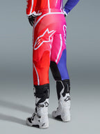 Alpinestars 2026 Fluid Apex bukser, motocross-bukser, flerfarvet rød, pink og lilla, set bagfra af kører iført bukser med hvide og sorte motocross-støvler, stort hvidt Alpinestars-logo, levende gradientdesign