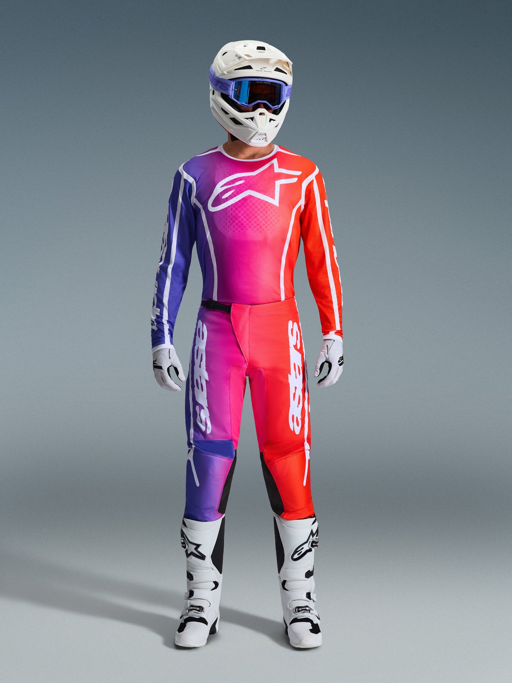 Motocrosskører iført 2026 Fluid Apex bukser og matchende jersey, lilla og orange gradient, hvid hjelm med goggles, hvide støvler og handsker, koordineret Alpinestars-racerudstyr til off-road kørsel.