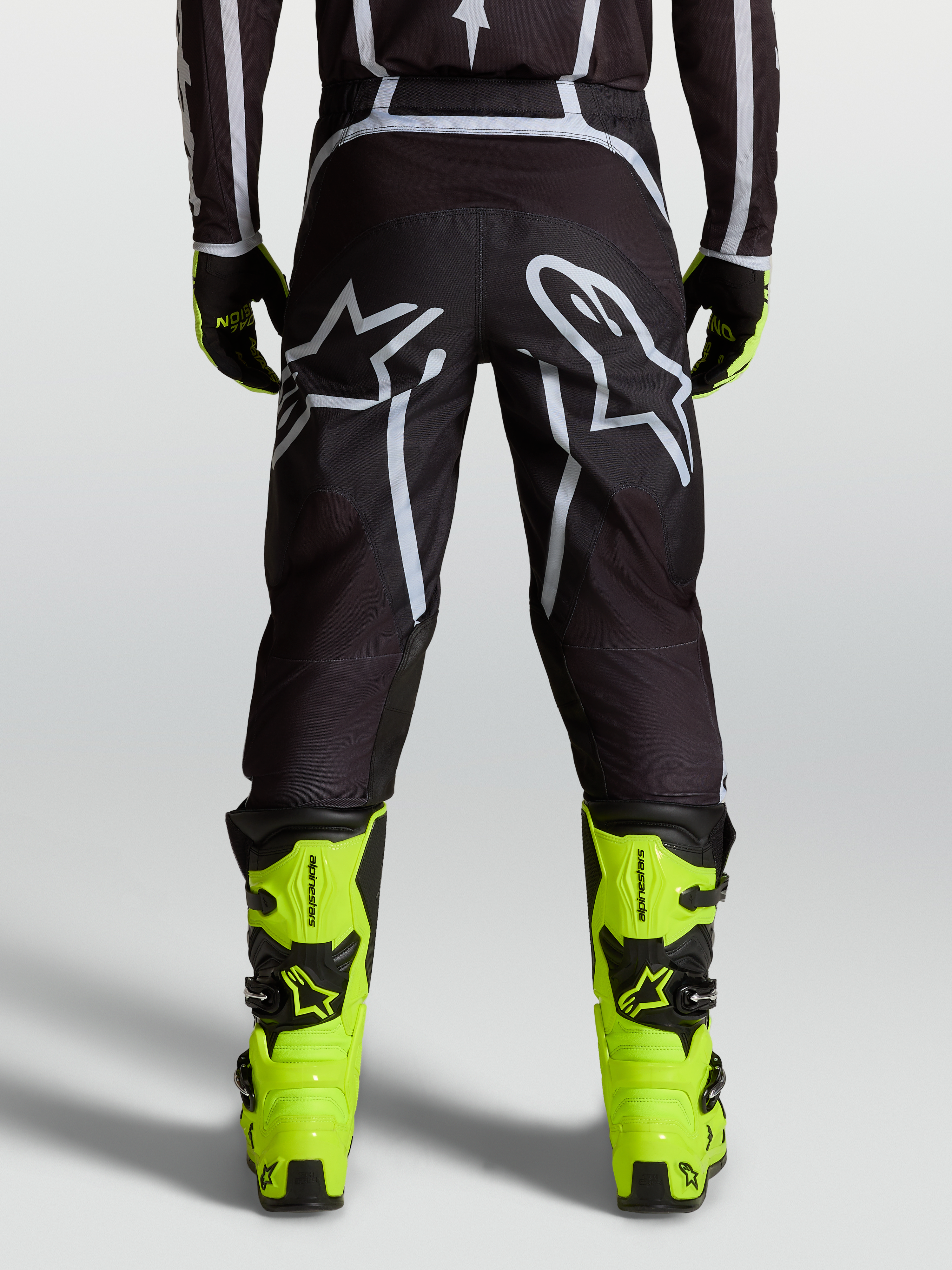 Alpinestars Fluid Apex V2 bukser, sort og sølv, herre motocrossbukser set bagfra med hvidt logo-grafik og gule støvler
