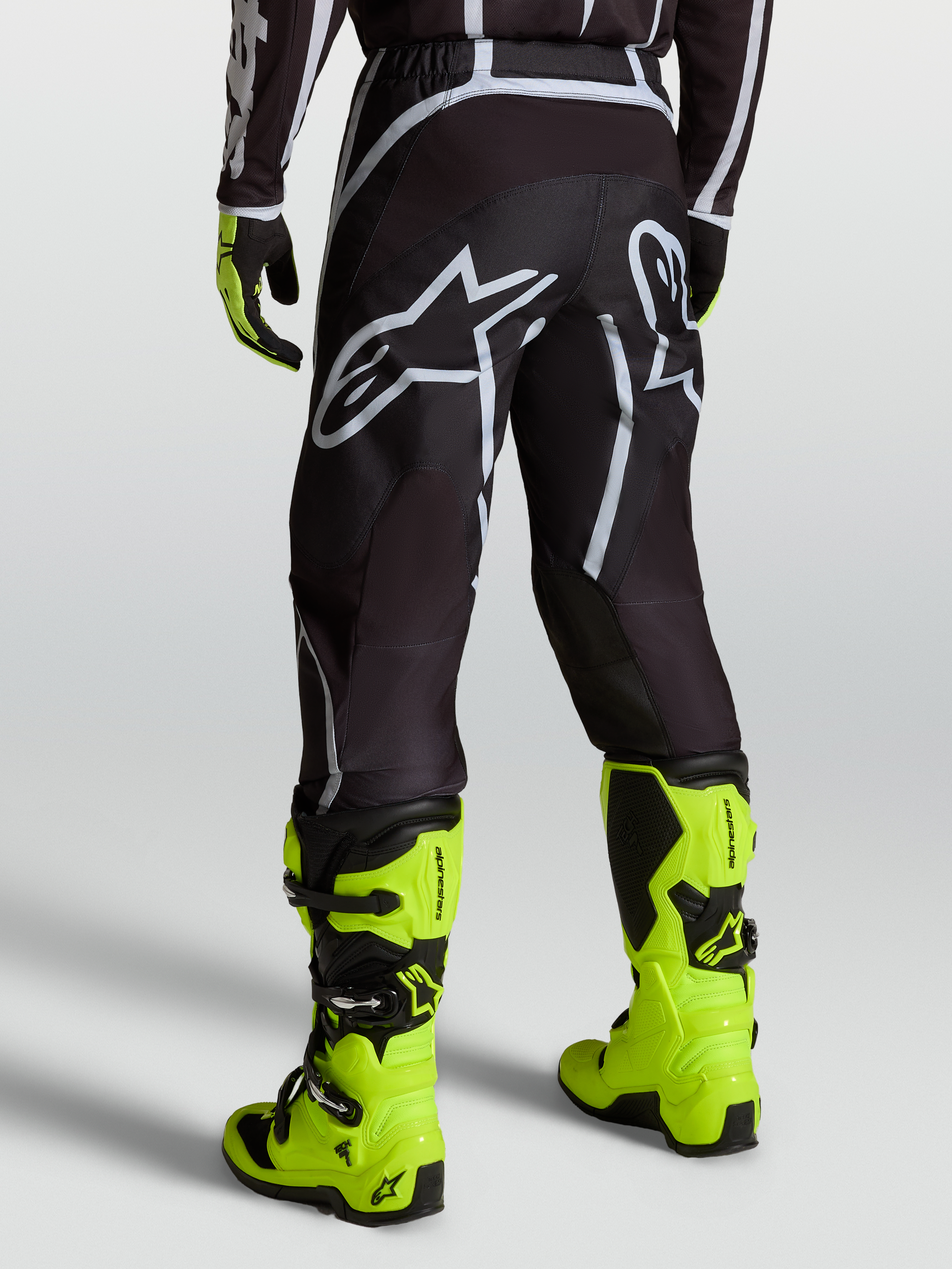 Alpinestars Fluid Apex V2 Bukser, motocrossbukser til mænd i sort og sølv, båret med gule støvler, bagfra