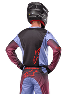 Alpinestars 2024 Racer Hoen-udstyr, motocrosskører set bagfra, Lavan Purple og sort jersey med rødt logo, matchende bukser med røde detaljer, sort hjelm, koordineret sæt til off-road racing