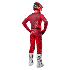 Alpinestars 2024 Racer Hoen-bukser og matchende trøje i Mars Red Burgundy, set bagfra af en motocross-kører i fuldt udstyr inklusiv rød hjelm og hvide støvler, der viser den atletiske pasform og branding til off-road kørsel.