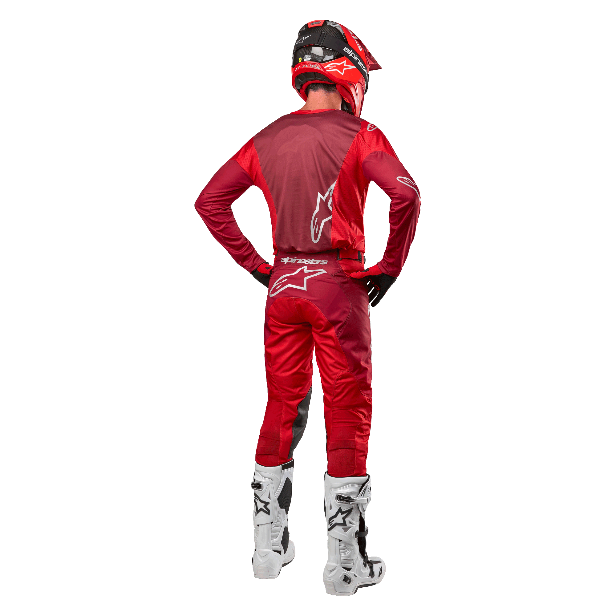 Alpinestars 2024 Racer Hoen-bukser og matchende trøje i Mars Red Burgundy, set bagfra af en motocross-kører i fuldt udstyr inklusiv rød hjelm og hvide støvler, der viser den atletiske pasform og branding til off-road kørsel.