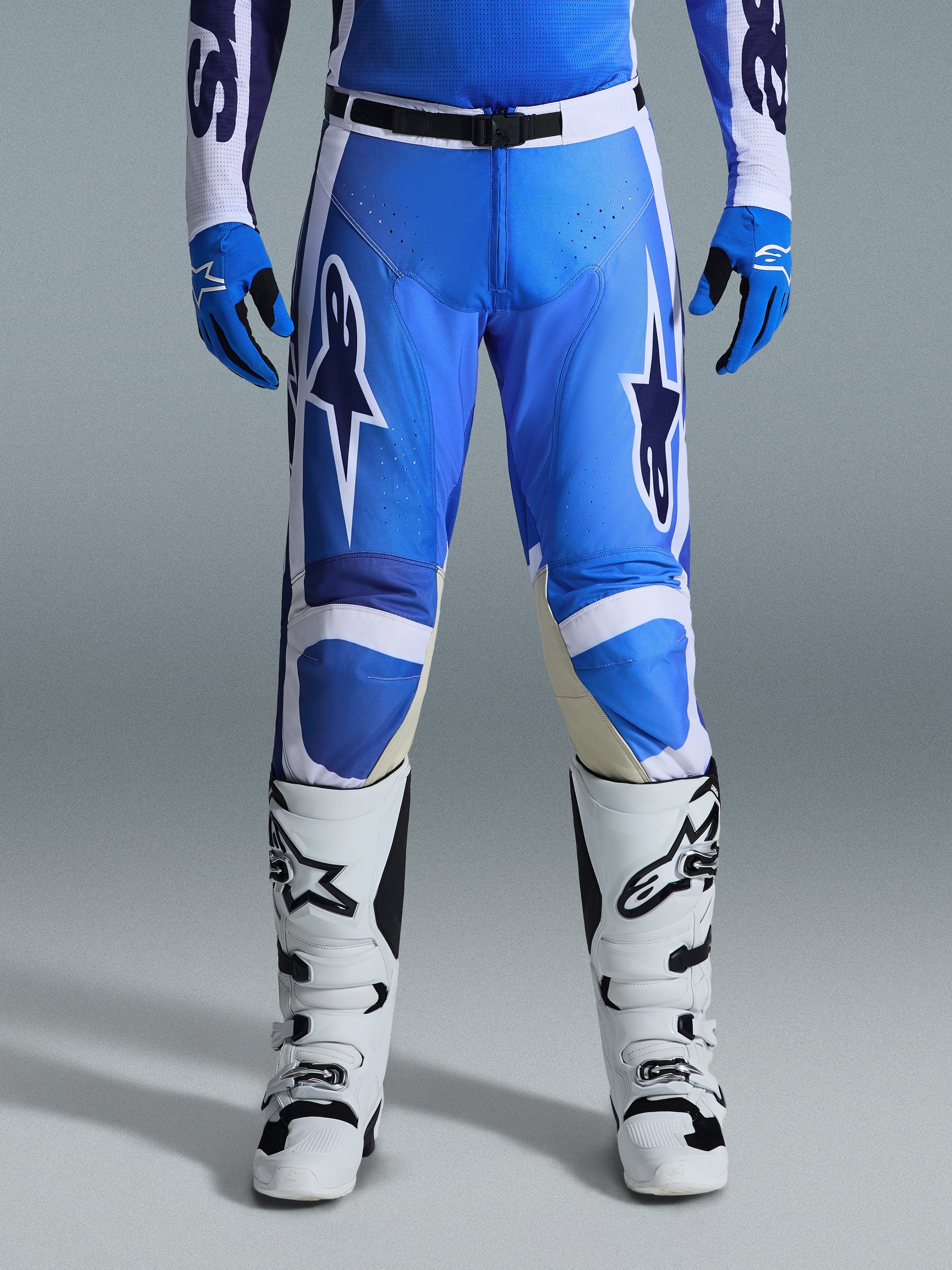 Alpinestars 2026 Racer Air Portl bukser, motocross-bukser, Ucla blå og hvid, båret med matchende blå handsker og hvide støvler, med sort taljelukning, store hvide stjernelogoer på lårene og perforeret stof for forbedret luftstrøm under off-road racing.