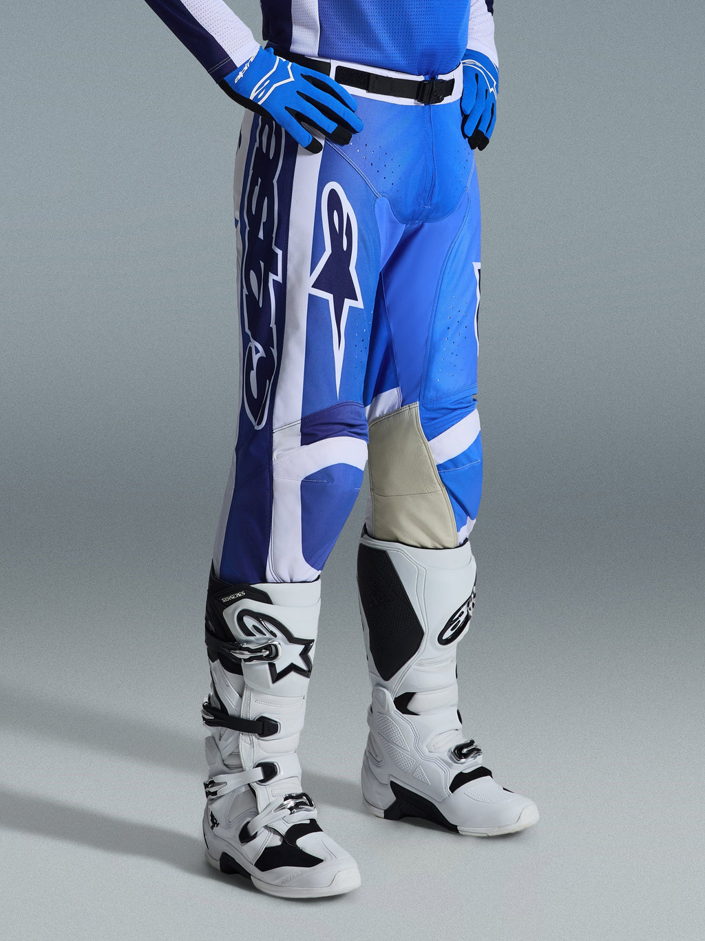 Alpinestars 2026 Racer Air Portl bukser, motocross-bukser, Ucla Blue og hvid, båret med matchende blå handsker og hvide og sorte motocross-støvler, med store hvide Alpinestars-logoer, lysebrune læderpaneler på indersiden af knæene og et sort magnetisk taljespænde.