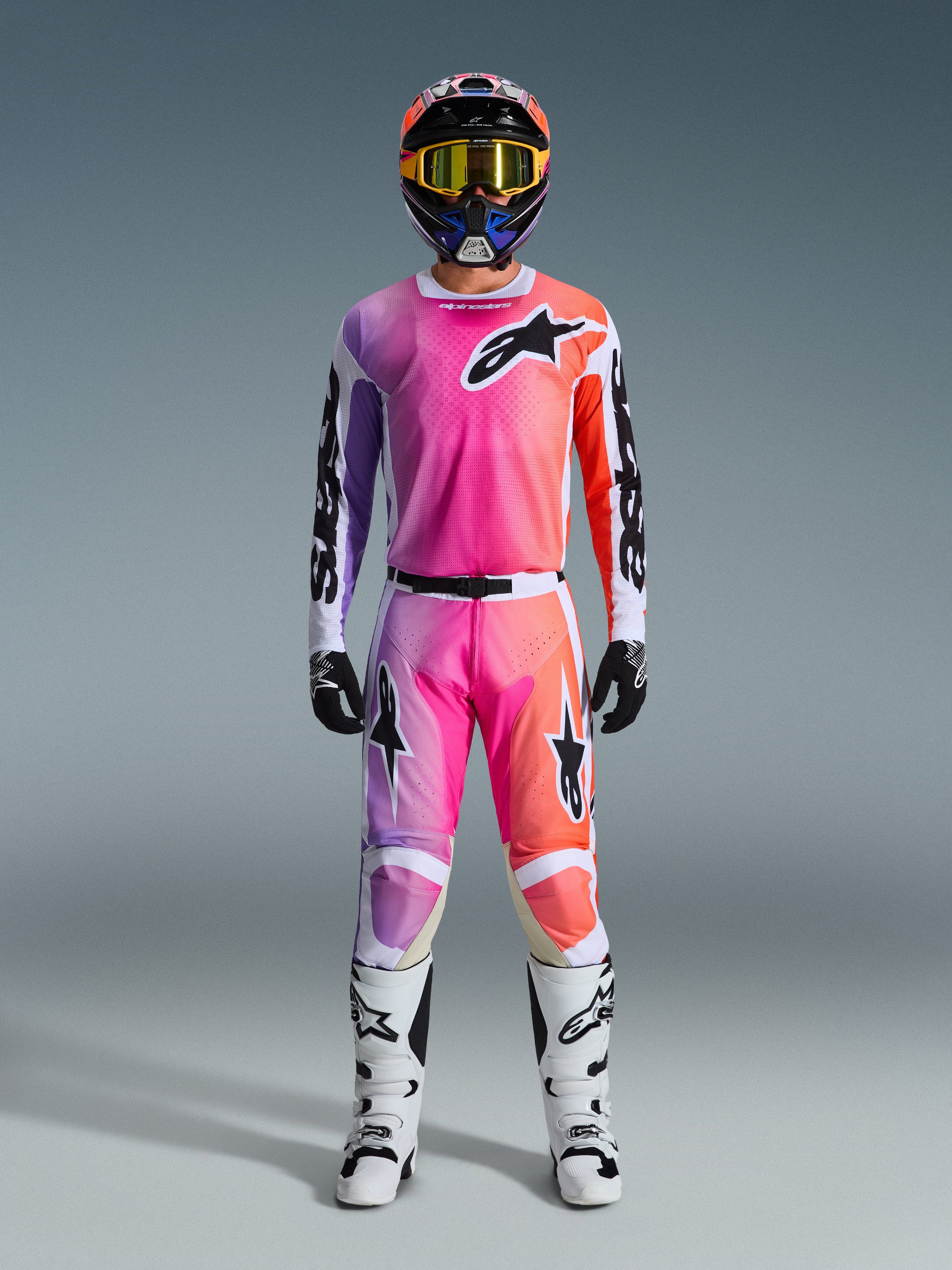Motocross-kører iført 2026 Racer Air Portl-trøje og matchende bukser, med en lyserød, lilla og orange gradient med sorte Alpinestars-logoer, hvide racingstøvler, sorte handsker og en flerfarvet hjelm, professionelt off-road racingudstyr.