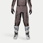 Alpinestars 2024 Fluid Lurv bukser, motocross-bukser, Mud Black, båret med matchende trøje, sorte handsker og hvide støvler, med store sorte logoer på lårene, ergonomisk pasform og slidstærkt materiale til off-road racing