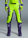 Alpinestars 2026 Supertech Vista bukser, motocross-bukser, fluorescerende gul, lilla og sort, båret med matchende handsker og lilla støvler, med store gradient-logoer på lårene, perforerede zoner til ventilation og et professionelt atletisk design til off-road racing