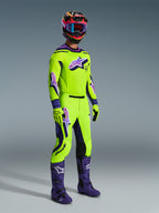 Alpinestars 2026 Supertech Vista udstyrssæt, professionel motocross-kører iført en stærk limegrøn trøje og bukser med lilla detaljer og logoer, matchende limegrønne handsker, lilla støvler og en flerfarvet hjelm med blå briller, koordineret atletisk udstyr til off-road racing