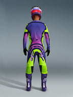 Alpinestars 2026 Supertech Vista-udstyrssæt, set bagfra af en motocrosskører iført en livlig lilla, lyserød og limegrøn gradueret racerdragt, med matchende trøje og bukser med iøjnefaldende branding, koordineret lilla og lyserød hjelm, lilla støvler og sorte handsker.