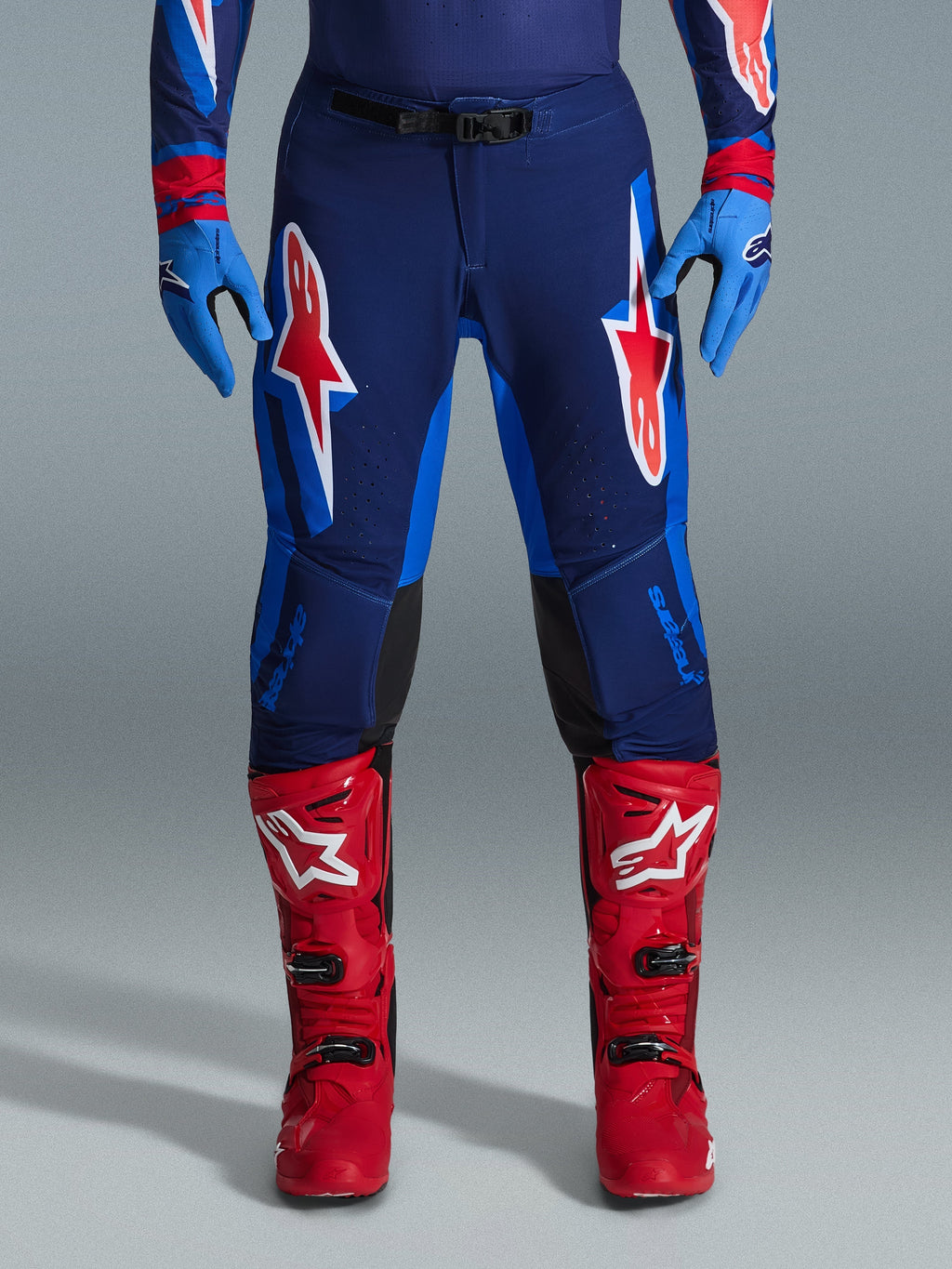 Alpinestars 2026 Supertech Vista bukser, motocrossbukser, Dark Navy, Hot Coral og Cobalt, set forfra af kører iført performance-udstyr med matchende blå handsker og røde motocrossstøvler, fremtrædende røde og hvide Alpinestars-logoer på lårene