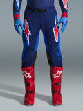 Alpinestars 2026 Supertech Vista bukser, motocrossbukser, Dark Navy, Hot Coral og Cobalt, set forfra af kører iført performance-udstyr med matchende blå handsker og røde motocrossstøvler, fremtrædende røde og hvide Alpinestars-logoer på lårene