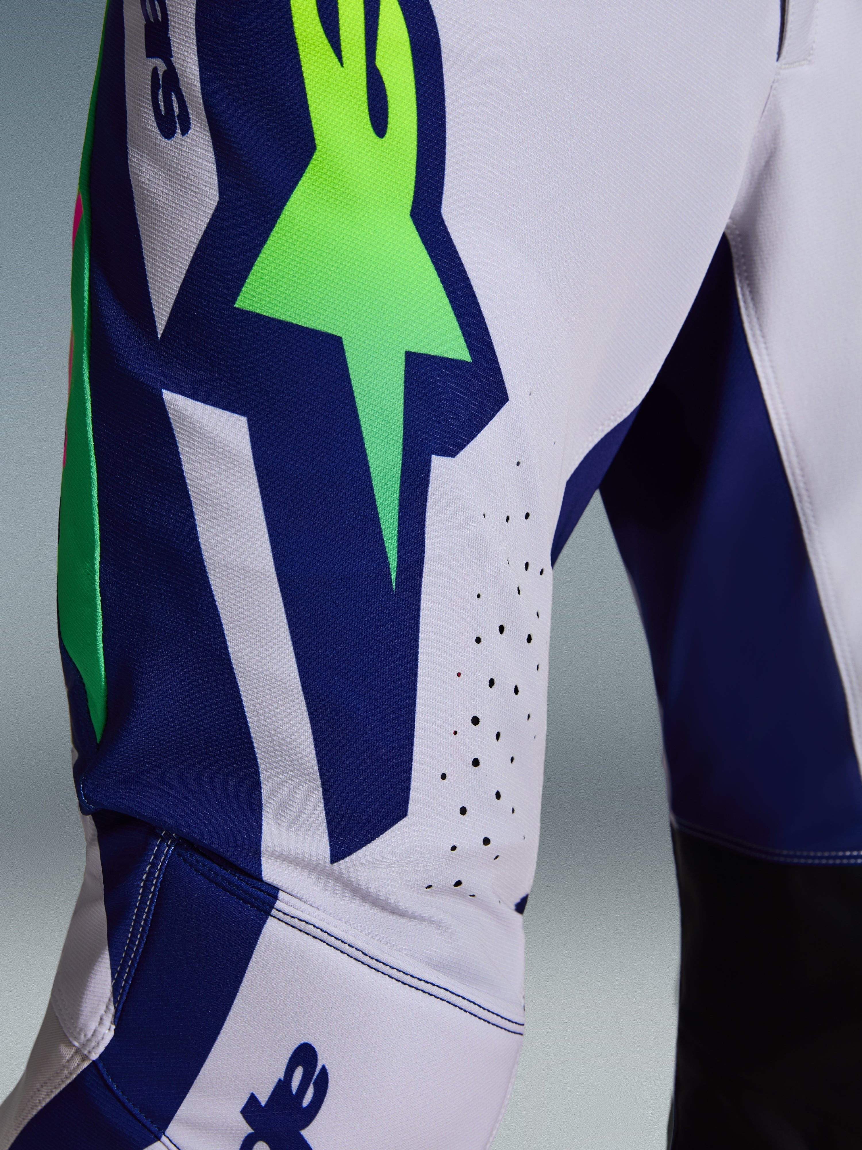 Alpinestars 2026 Supertech Vista bukser, motocrossbukser, lysegrå med Yellow Fluo og blå detaljer, nærbillede af låret der viser det store A-star logo, laserskårne ventilationshuller og avanceret stræk-ripstop-stof.