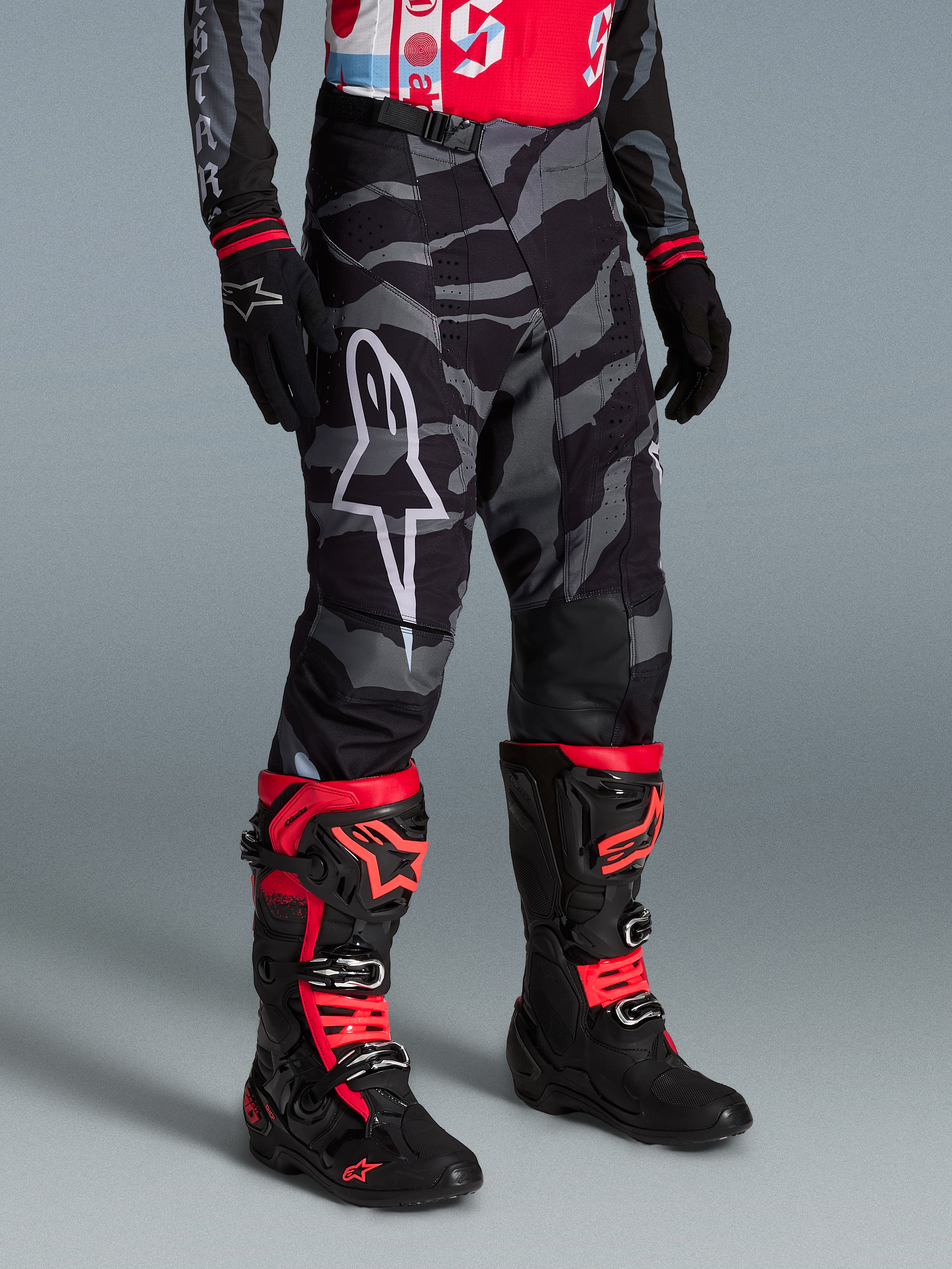 Alpinestars Techstar Beast Coast bukser i grå camouflage, vist med sorte og røde motocross-støvler til off-road kørsel.