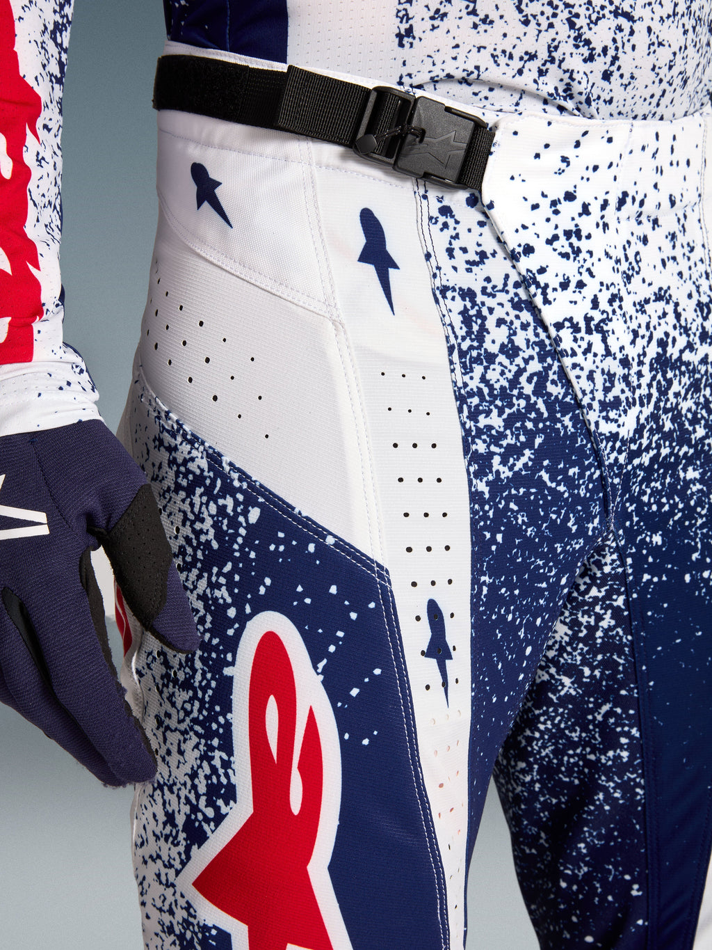 Alpinestars Techstar Unity motocrossbukser i blå og hvid med spættet mønster, rødt logo og SX2 magnetisk spænde.