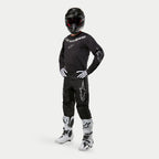 Alpinestars 2024 Fluid Graphite Pants, Motocross Pants, Black and Silver, worn with matching black jersey, black helmet, white gloves, and white boots, featuring silver Alpinestars logos on the thighs, ergonomic athletic fit for off-road racing.