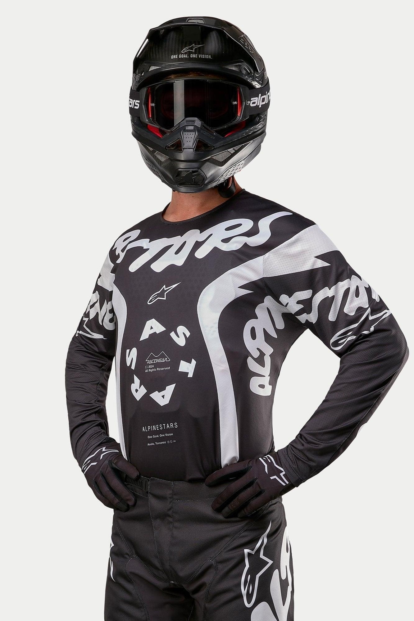 Alpinestars 2024 Racer Hana trøje, motocross-trøje, sort og hvid, med markant hvid Alpinestars-tekstgrafik og logo, båret af en kører med sort hjelm og goggles, højtydende udstyr til off-road racing