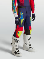 Alpinestars 2027 Fluid Drag bukser til ungdom, marineblå og røde motocrossbukser med neondetaljer og hvide motocrossstøvler.