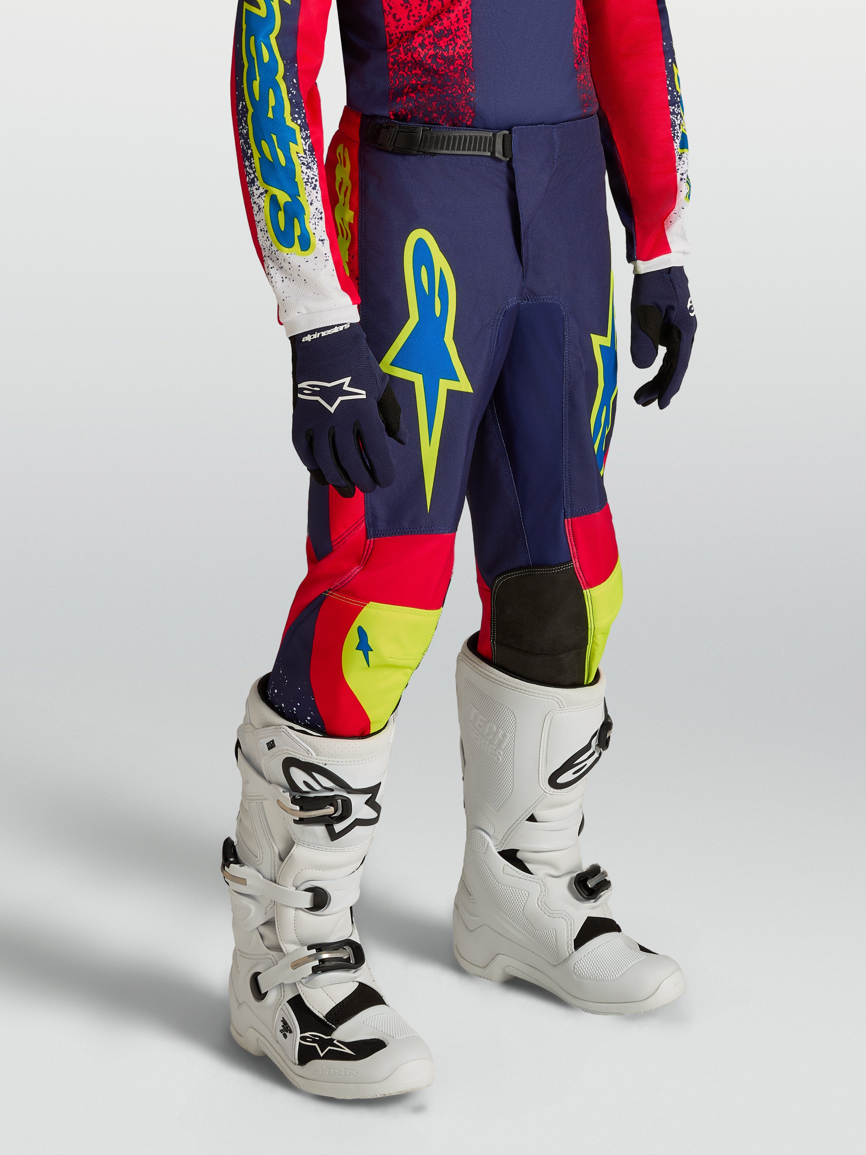 Alpinestars 2027 Fluid Drag bukser til ungdom, marineblå og røde motocrossbukser med neondetaljer og hvide motocrossstøvler.