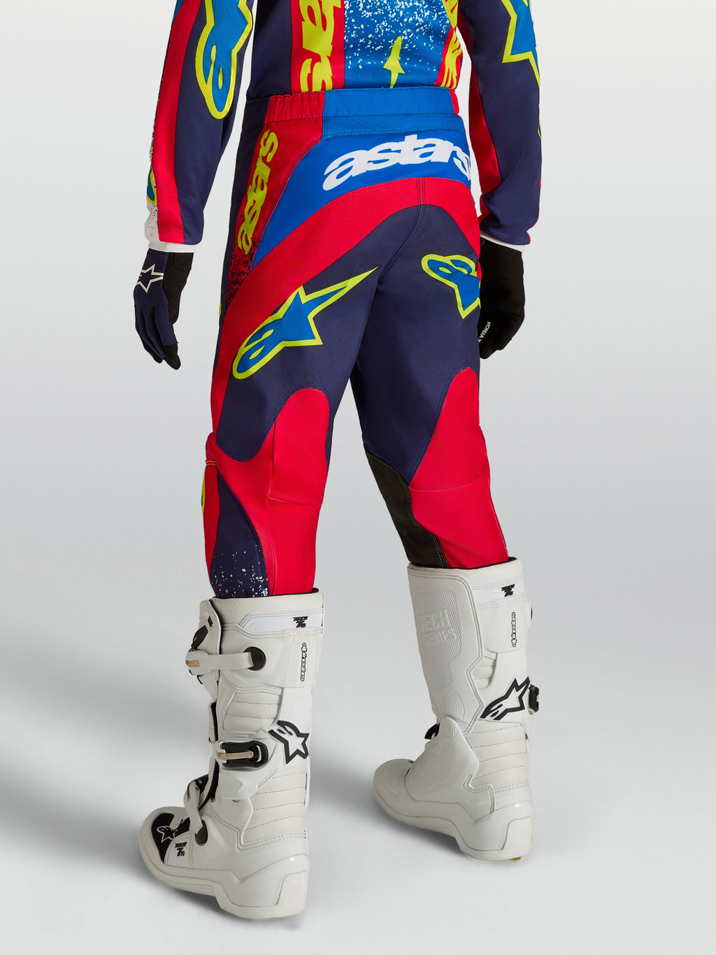 Alpinestars 2027 Fluid Drag Bukser Ungdom, motocrossbukser i blå og rød, set bagfra med hvide støvler.