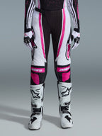 Alpinestars 2026 Stella Techstar Nomur bukser til kvinder, motocross-bukser, sort, hvid og fuchsia, båret med matchende racertrøje, handsker og hvide motocross-støvler, med markant pink grafik og astars-logoer på knæene, designet til off-road-konkurrence på højt niveau