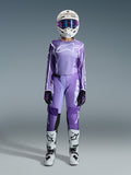 Motocross-rytter i Alpinestars 2026 Stella Fluid Apex-udstyrssæt til kvinder, violet og hvid jersey med matchende bukser, hvid hjelm med lyserøde goggles og hvide og sorte off-road støvler, komplet racersæt til motocross til kvinder.