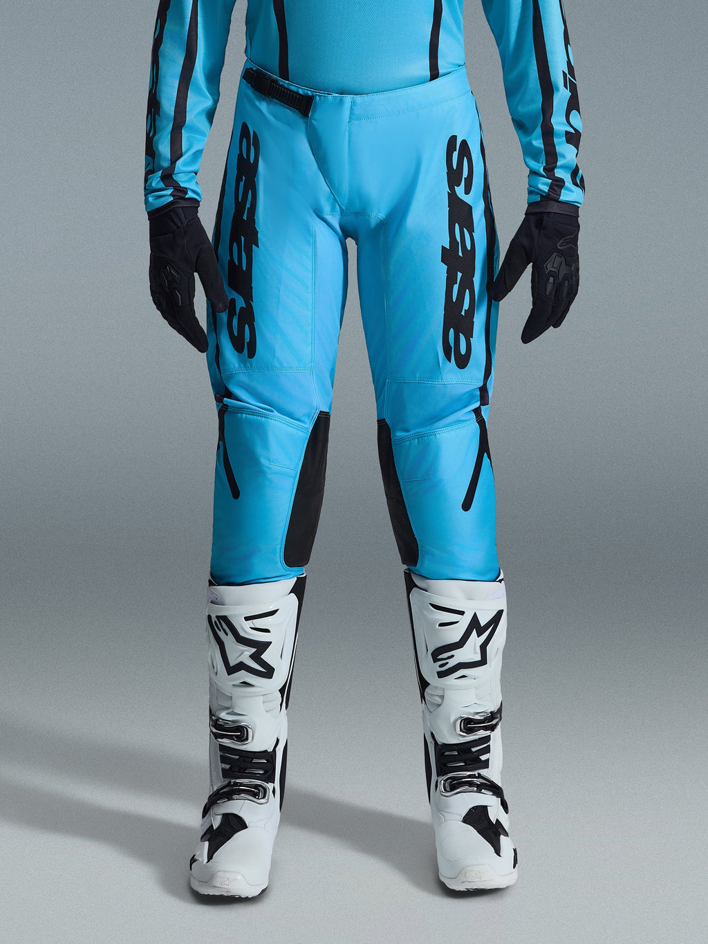 Alpinestars 2026 Stella Fluid Apex bukser til damer, motocrossbukser, klar cyan og sort, lodret sort branding på lårene, sorte forstærkede indvendige knæpaneler, vist med hvide og sorte motocross-støvler og sorte handsker, professionelt off-road-udstyr til kvinder