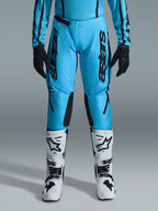 Alpinestars 2026 Stella Fluid Apex bukser til damer, motocrossbukser, klar cyan og sort, lodret sort branding på lårene, sorte forstærkede indvendige knæpaneler, vist med hvide og sorte motocross-støvler og sorte handsker, professionelt off-road-udstyr til kvinder