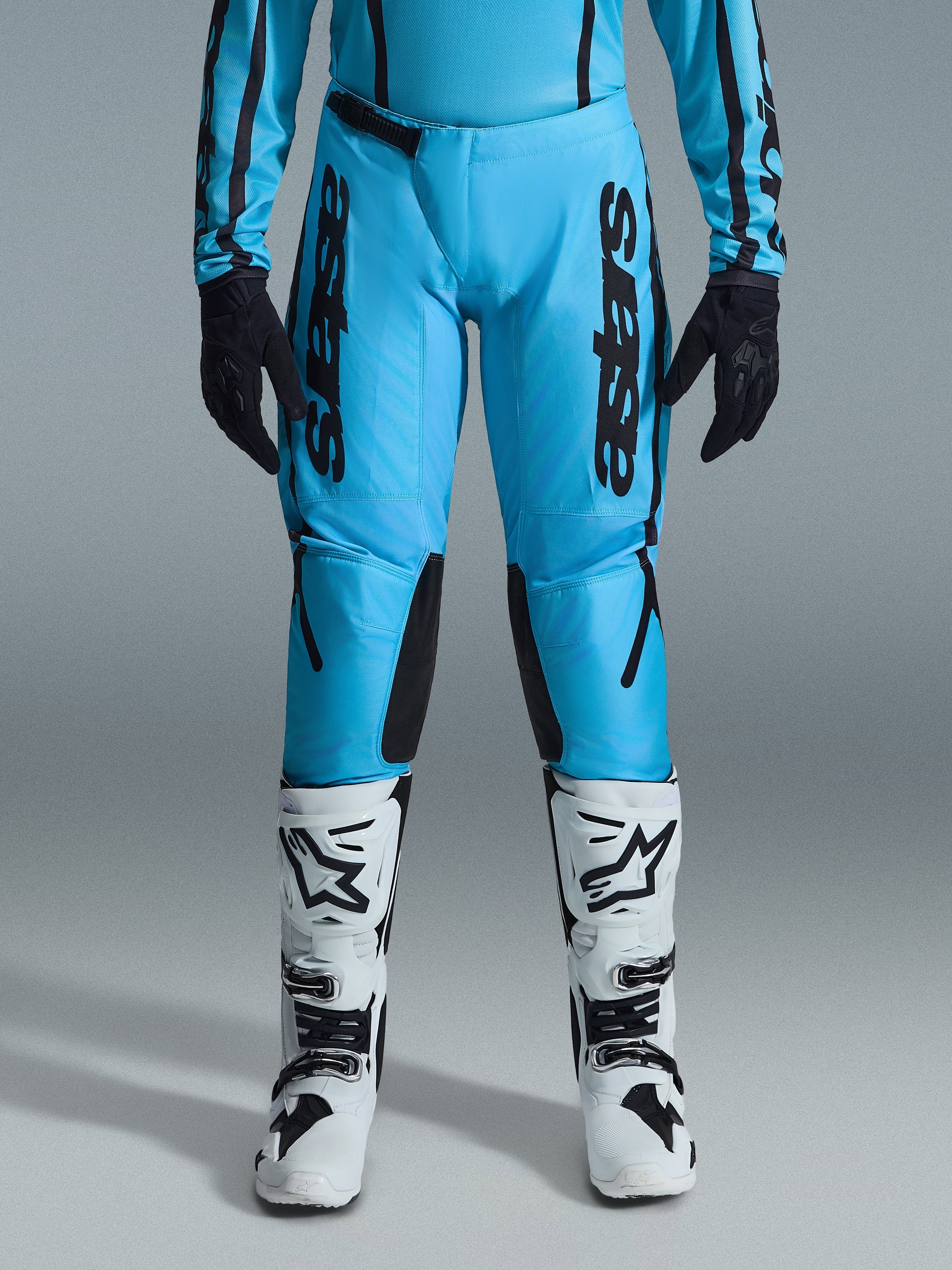 Alpinestars 2026 Stella Fluid Apex bukser til damer, motocrossbukser, klar cyan og sort, lodret sort branding på lårene, sorte forstærkede indvendige knæpaneler, vist med hvide og sorte motocross-støvler og sorte handsker, professionelt off-road-udstyr til kvinder