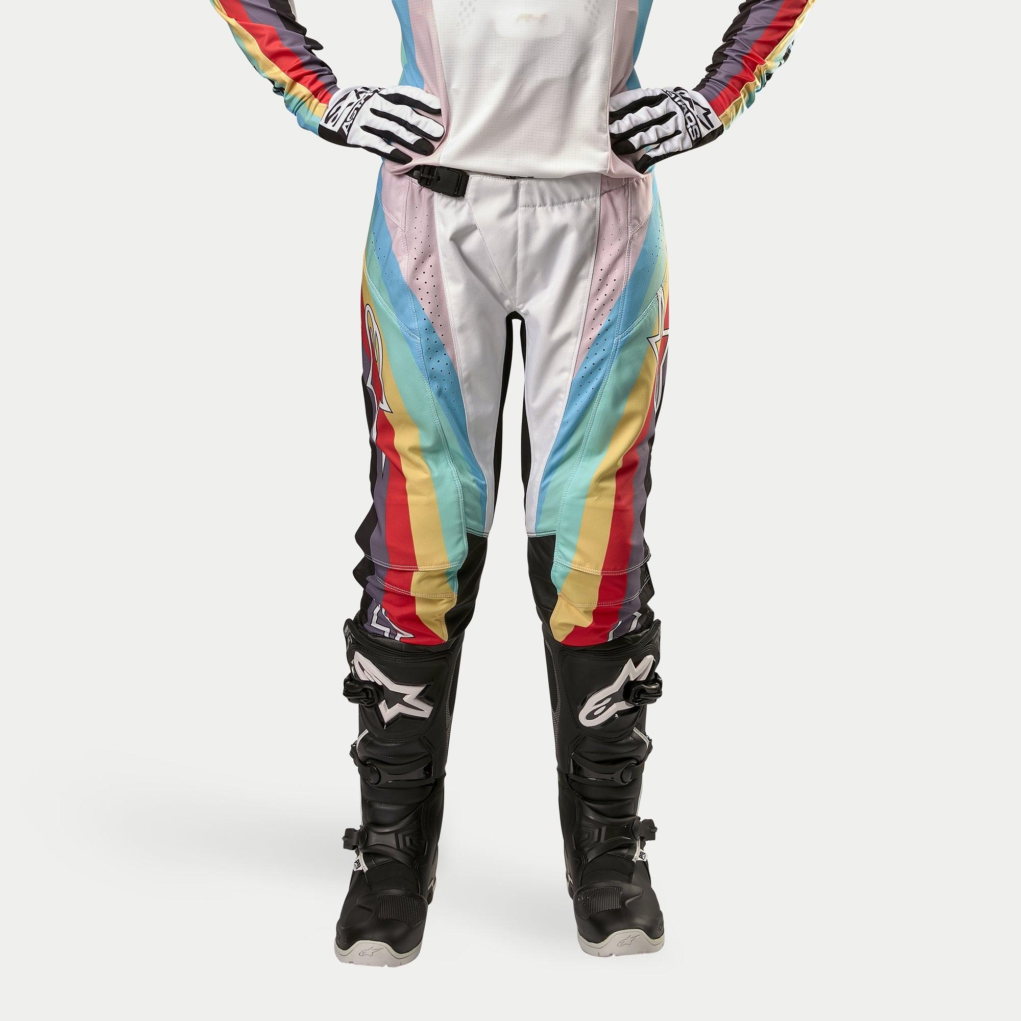 Alpinestars Stella 2024 Techstar bukser til damer, motocrossbukser, sort multifarvet med livlige diagonale striber i hvid, blå, rød og gul, vist med sorte motocrossstøvler og handsker, racerinspireret design til terrænkørsel