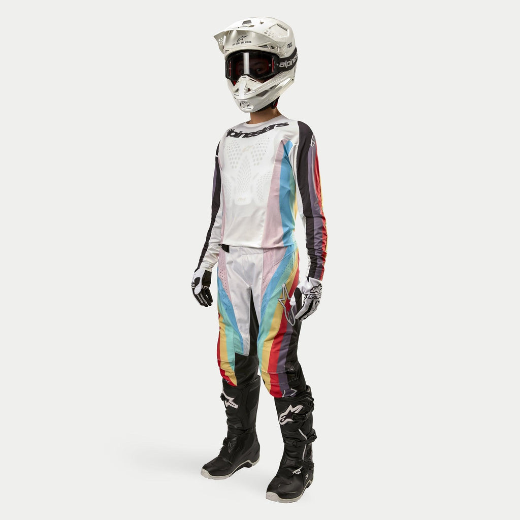Motocross-kører iført Alpinestars Stella 2024 Techstar bukser til kvinder, motocrossbukser, sort flerfarvet med hvide paneler og farverige diagonale striber, matchende trøje, hvid hjelm og sorte støvler, koordineret off-road racerudstyr til kvinder