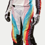 Alpinestars Stella 2024 Techstar bukser til damer, motocross-bukser, sort multifarvet med livlige diagonale striber i blå, pink, gul og rød, med et stort stjernelogo på låret, vist iført matchende trøje og handsker, professionelt terrænkørselsudstyr