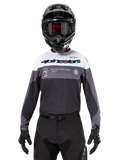 Motocross-rytter iført Alpinestars Pro-Dura Jersey i Black Magnet White, langærmet performance-trøje med hvide og grå farveblokke, bæres med sort hjelm og goggles, med 'alpinestars' branding og 'ONE GOAL ONE VISION' slogan, off-road motorcykel-racingudstyr