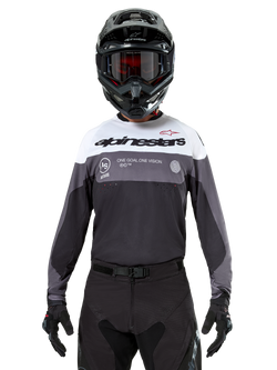 Motocross-rytter iført Alpinestars Pro-Dura Jersey i Black Magnet White, langærmet performance-trøje med hvide og grå farveblokke, bæres med sort hjelm og goggles, med 'alpinestars' branding og 'ONE GOAL ONE VISION' slogan, off-road motorcykel-racingudstyr