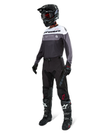 Alpinestars Pro-Dura Jersey i Black Magnet White, båret af en motocross-kører i fuldt gear, inklusive sorte bukser, sort hjelm med goggles og sort-hvide støvler. Jerseyen har et teknisk farveopdelt design med hvide, grå og sorte paneler, skabt til enduro- og off-road-performance.