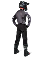 Motocross-kører iført Alpinestars Pro-Dura Jersey i Black Magnet White, set bagfra med gråt mesh-rygpanel og sorte ærmer med hvid Alpinestars-branding, koordineret med sorte bukser, sort hjelm og sort-hvide støvler, professionelt enduro-racerudstyr