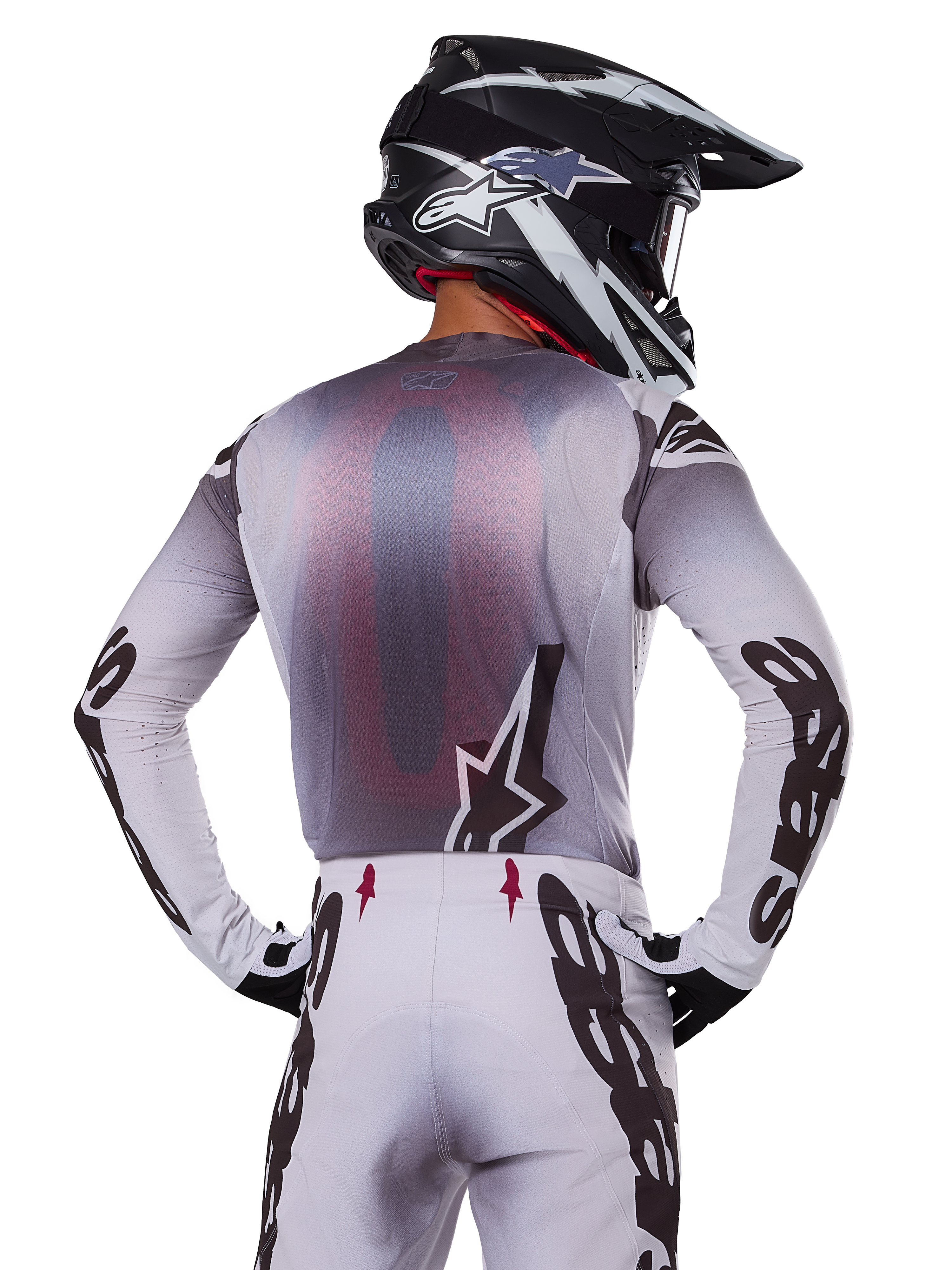 Motocrossrytter set bagfra iført Alpinestars 2025 Supertech Maker Jersey, sølv og sort med rødt mesh-rygpanel og sorte logoer på ærmerne, kombineret med matchende motocrossbukser og en sort og hvid hjelm, professionelt off-road racerudstyr