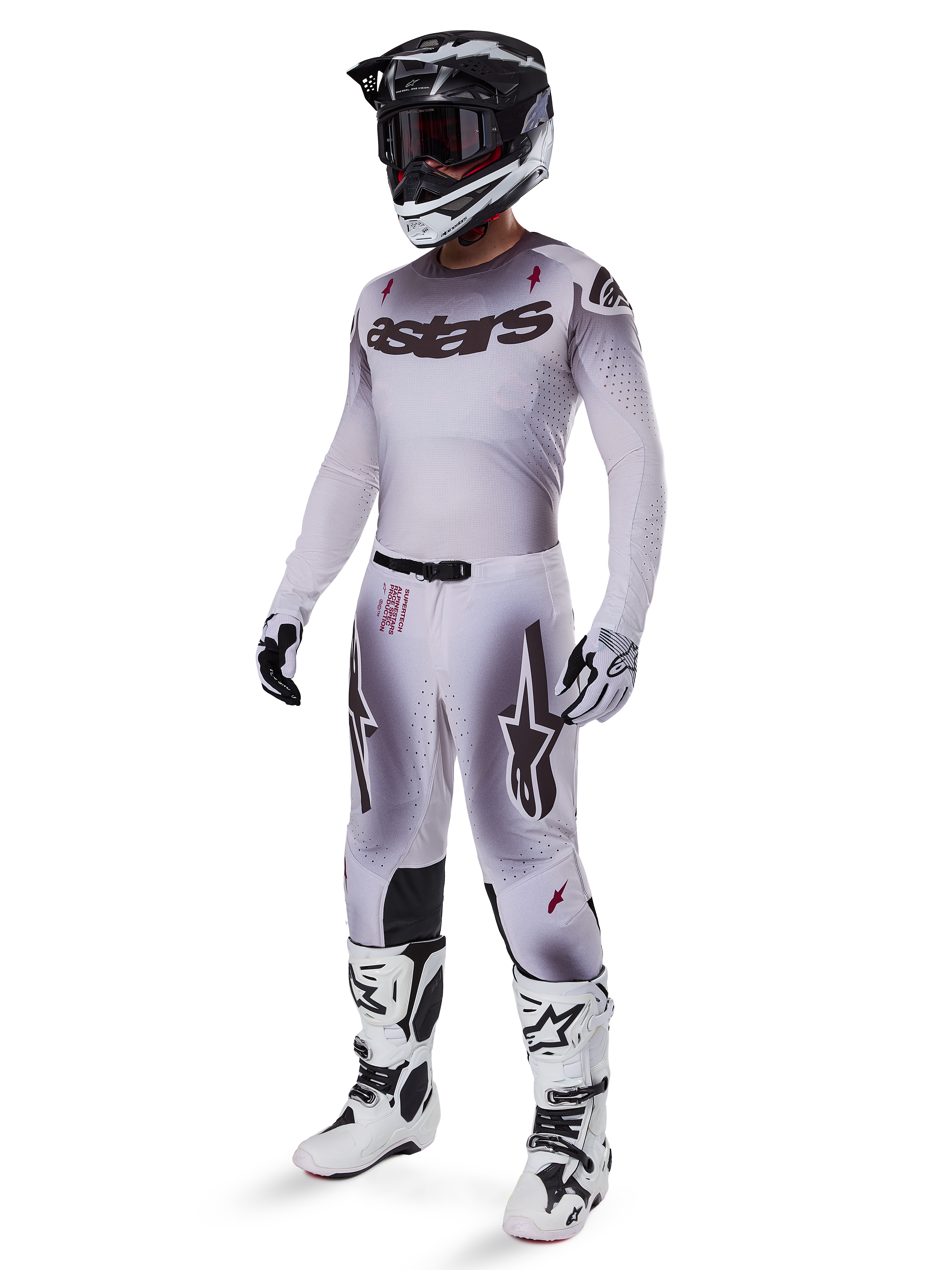 Motocrossrytter iført 2025 Supertech Maker-bukser i Silver Black, koordineret med en matchende sølv og grå jersey, sort og hvid hjelm samt hvide racingstøvler, med teknisk atletisk pasform til professionel terrænkørsel.