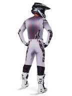 Motocrosskører set bagfra iført Alpinestars 2025 Supertech Maker bukser i sølv og sort, matchende langærmet jersey, sort og hvid hjelm og hvid-sorte støvler, med markant sort branding på benene, professionelt off-road racerudstyr